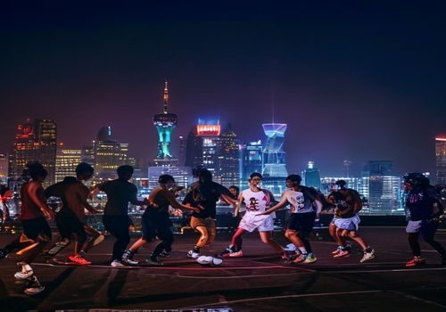 男人团成员在上海举行线下篮球友谊赛，十余名男性在球场上激烈对抗，背景为城市夜景灯光